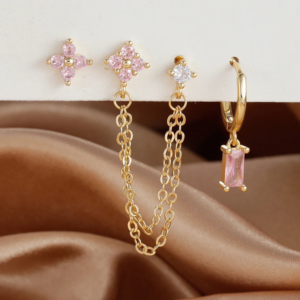 Set of gold earrings with pink gemstones on a beige surface