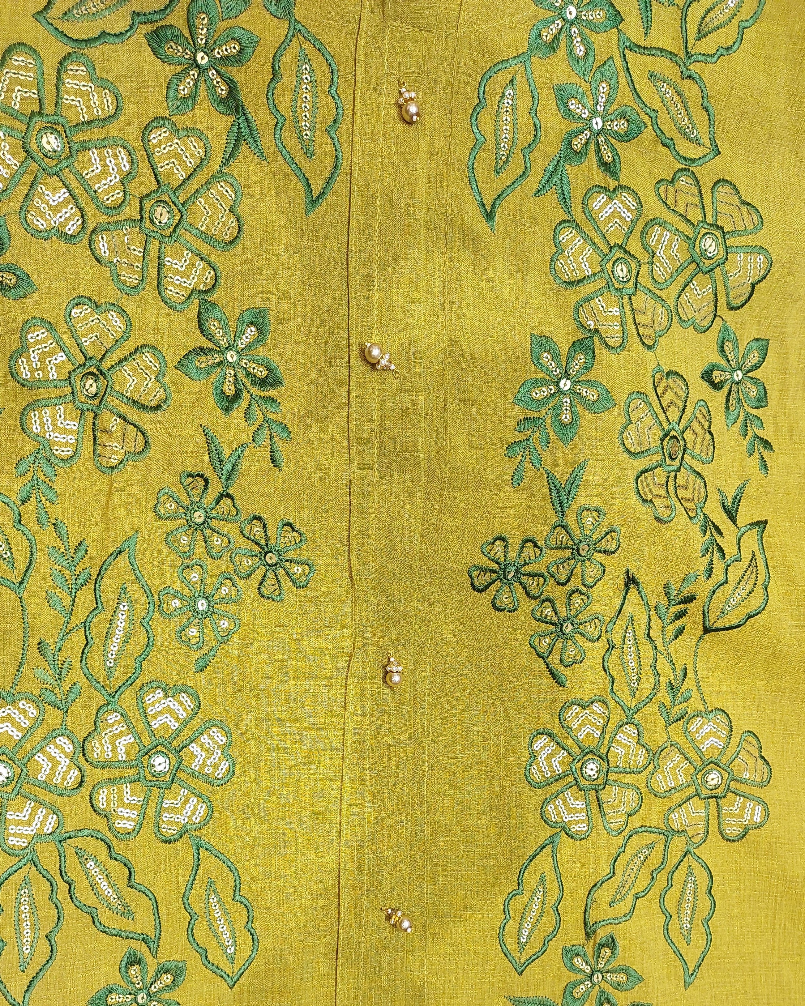 Close-up of a green embroidered garment with floral patterns on a yellow background